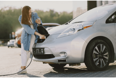 Mulher segurando um celular enquanto conecta o carro elétrico ao carregador.