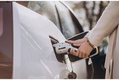 Mãos de uma mulher conectando um carro elétrico ao carregador. 