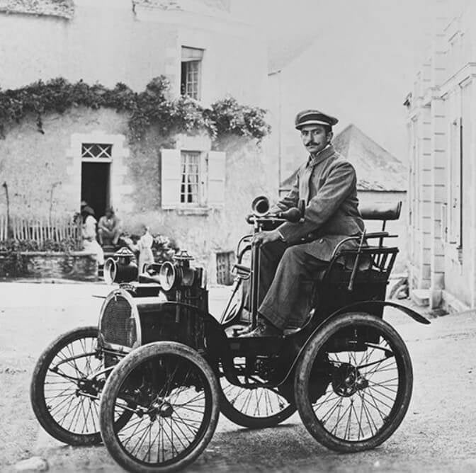 Fotografia em preto e branco mostra Louis Renault, criador da montadora Renault, em cima do seu triciclo.