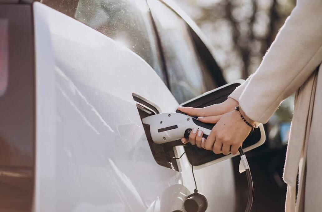 Mãos de uma mulher conectando um carro elétrico ao carregador. 